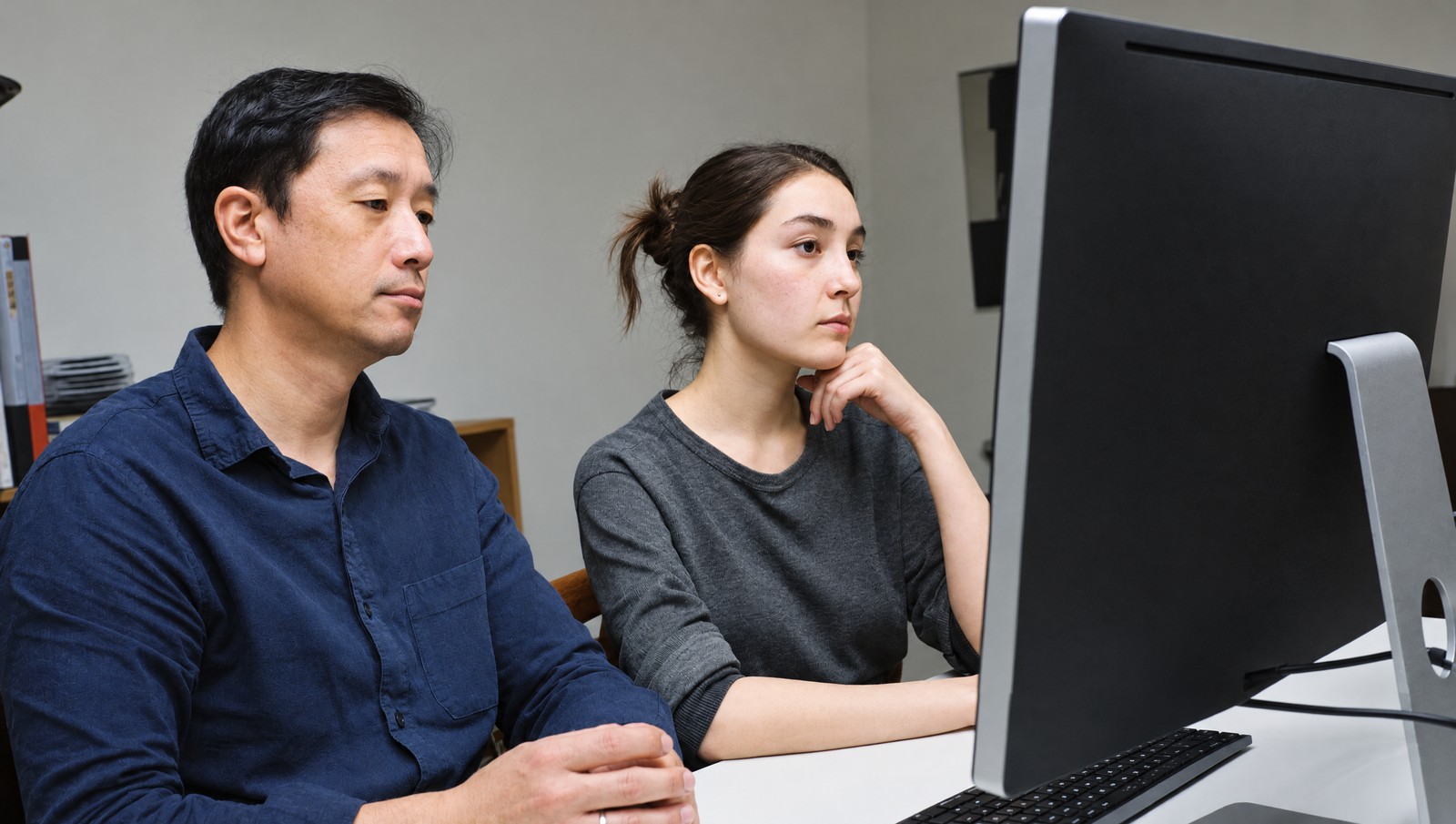 Photographic illustration of two people reviewing work together at a desktop computer