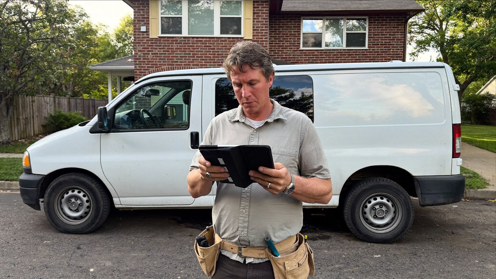 Photographic illustration of a plumbing business owner reviewing a tablet beside a plain service van