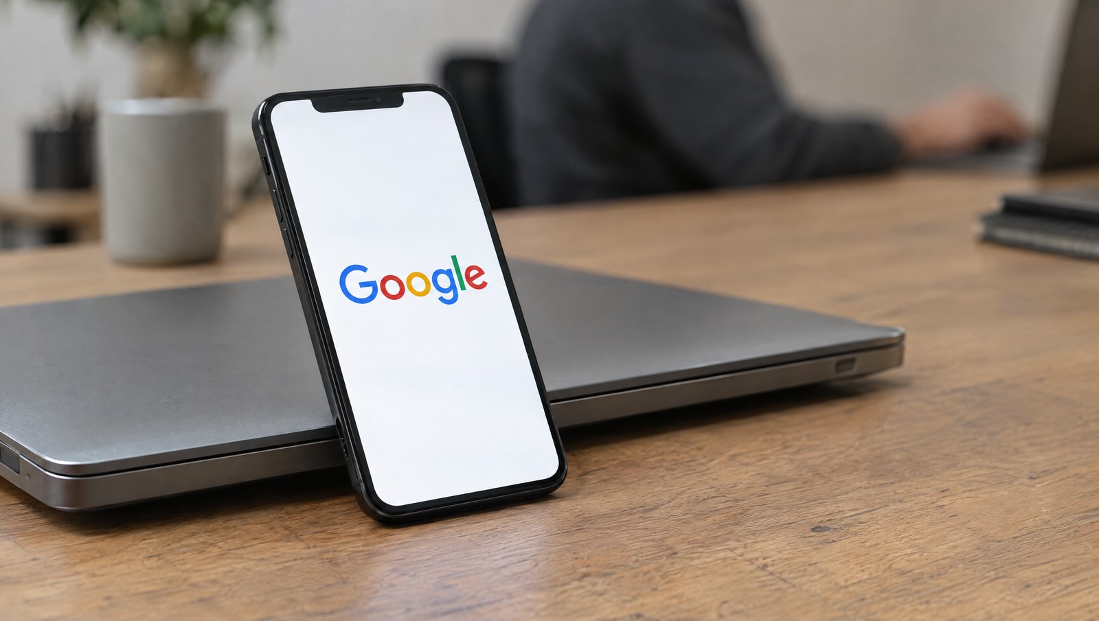 Photographic illustration of the Google wordmark on a smartphone beside a closed laptop